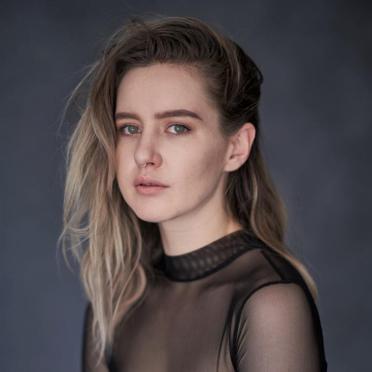 AVAXA in a black top against a blue grey background posing for a photo