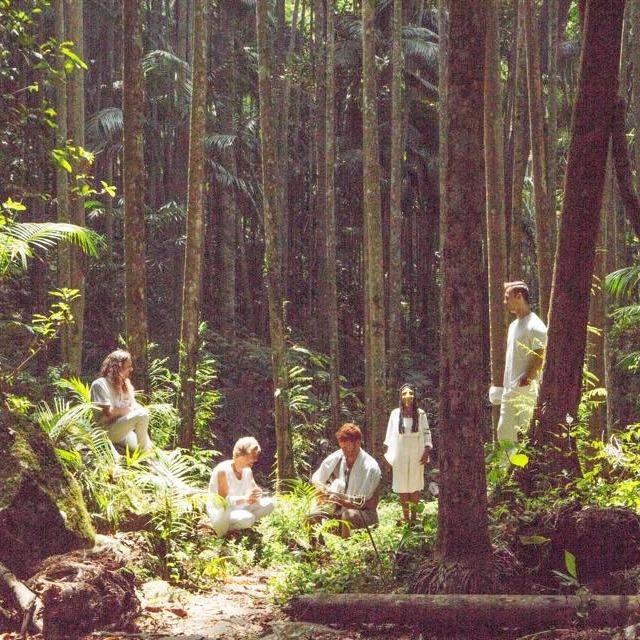 Endless Valley in white attire standing in the forest surrounding by green foliage and large trees.