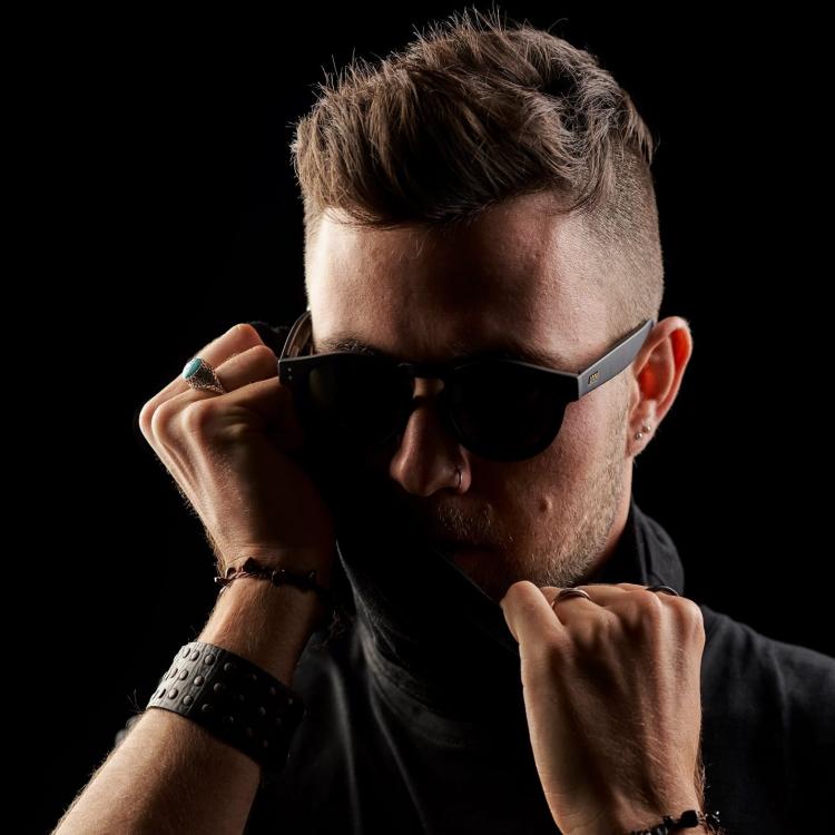 ZigMon wear glasses holding his collar in front of a black background