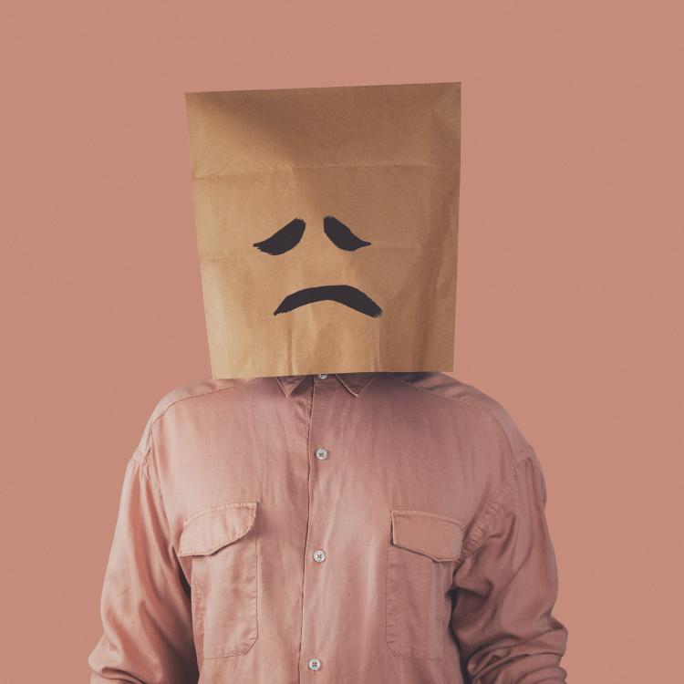 sad face. in a pink shirt with a sad paper bag on his head in front of a pink background