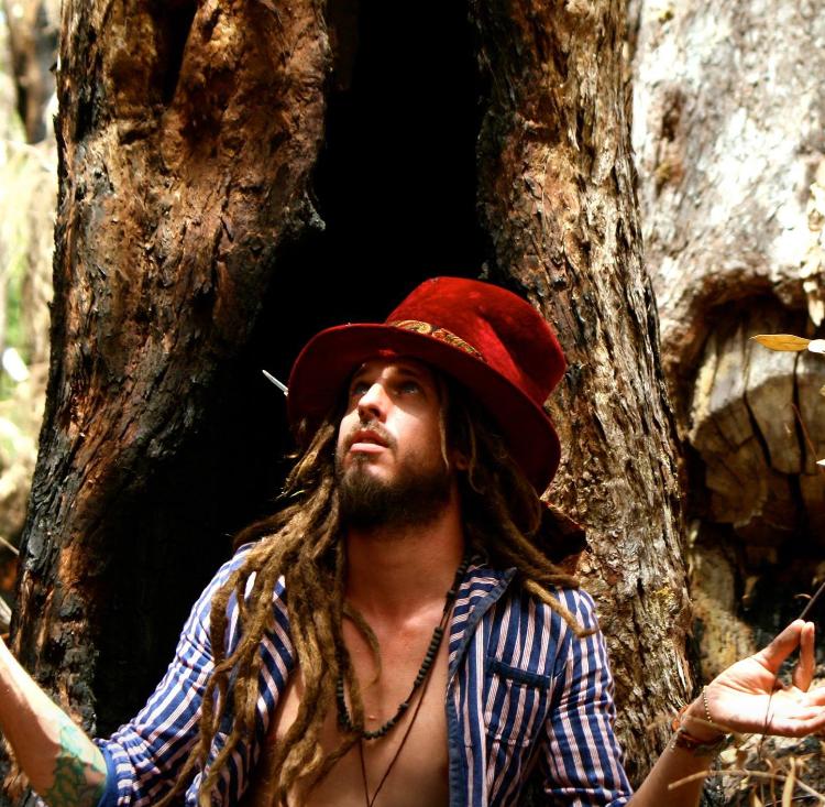 Leatherlab sitting in front of a tree with an open blue and white stripe shirt on wearing a red top hat.
