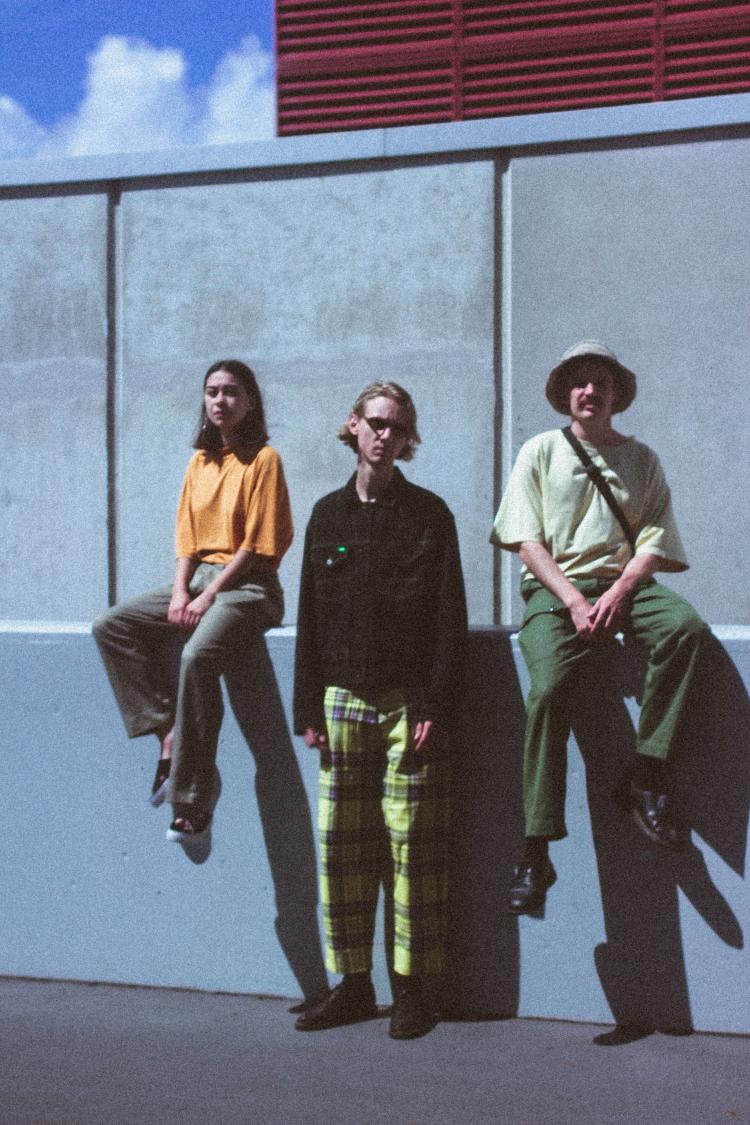 3 members of Mon Riser sitting on a concrete ledge wearing alternative wear.