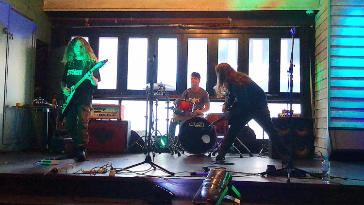 The 3 members of Stray Dog Saviours playing a live show with the guitarist on the left, drummer in the middle and the bass player in a rock pose on the right.
