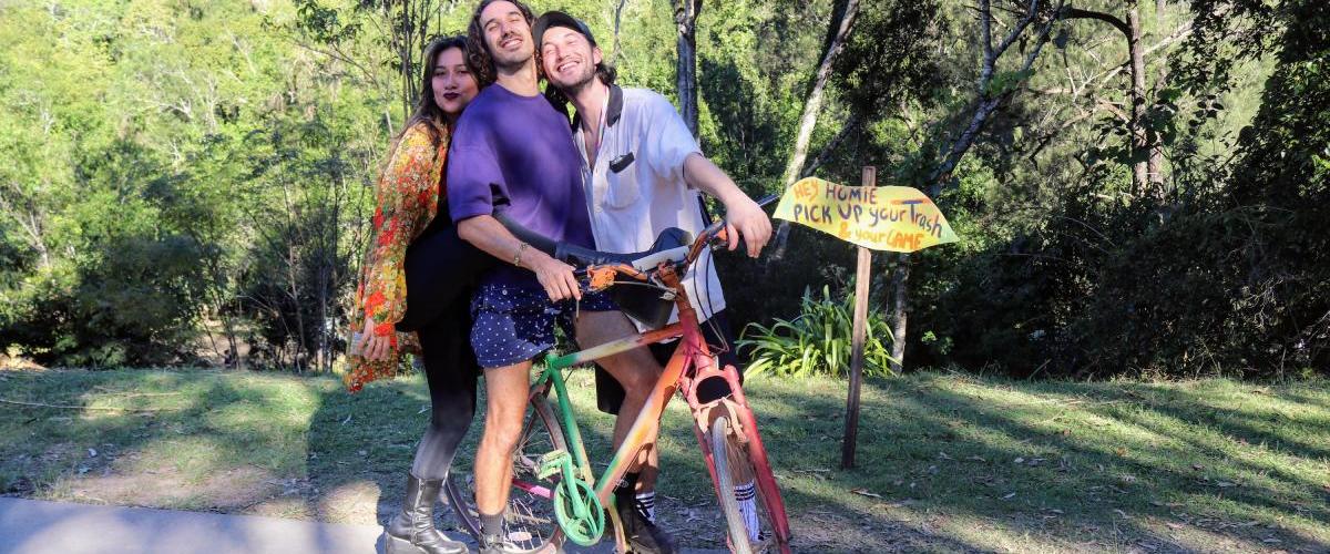 Three people sitting on a rainbow bicycle smiling enthusiastically